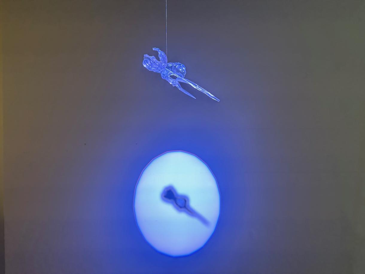Image of a clear 3d printed iris flower, illuminated by blue light, with a shadow projected on a wall behind the flower